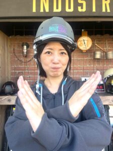 あごひもを締めずにヘルメットを被り胸の前でバツ印を作っている